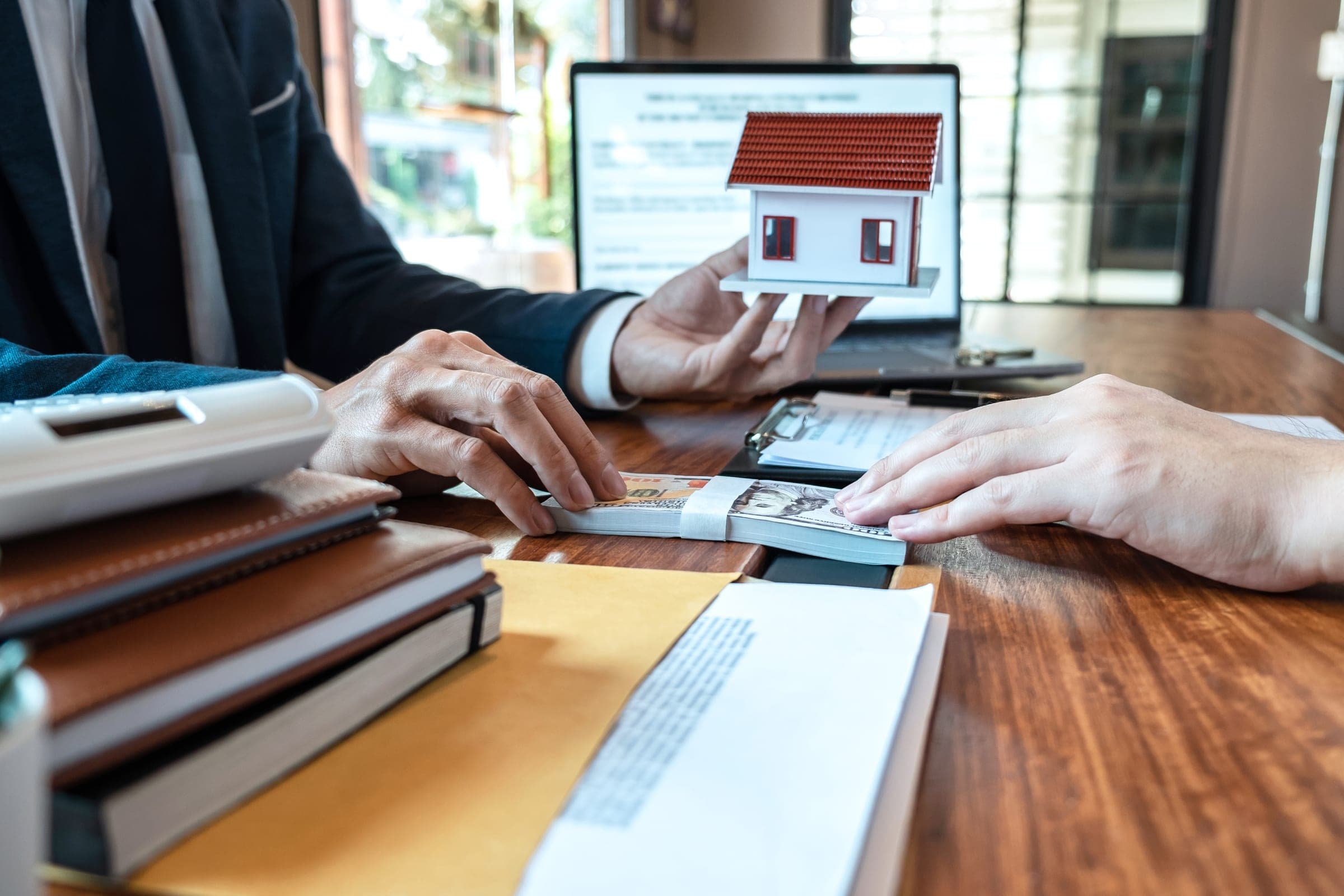 Hands exchanging documents for in-specie transfer in SMSF with model house and laptop.