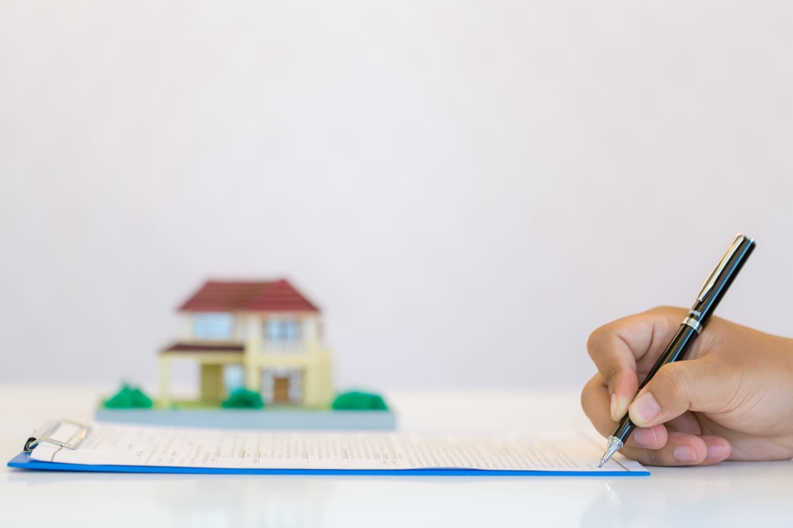 A hand signing a loan document beside a model house