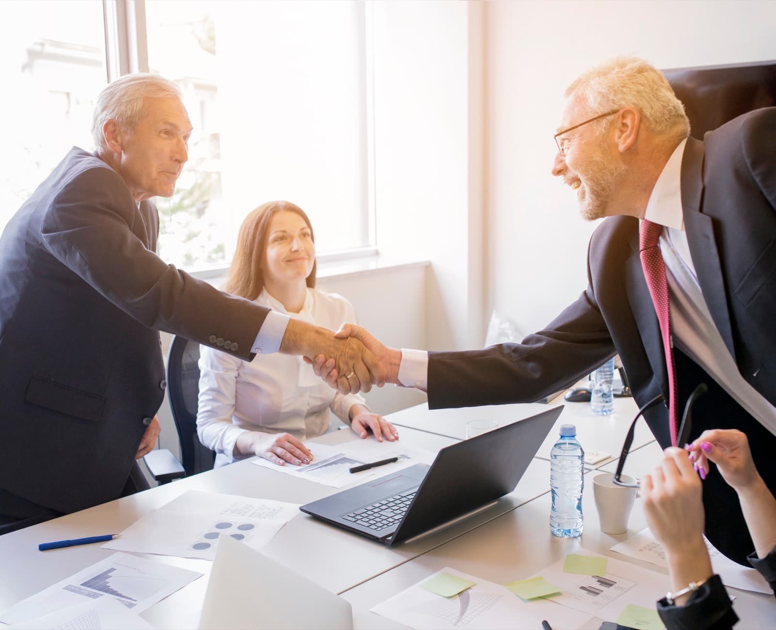 Two people shaking hands over an agreement at a desk