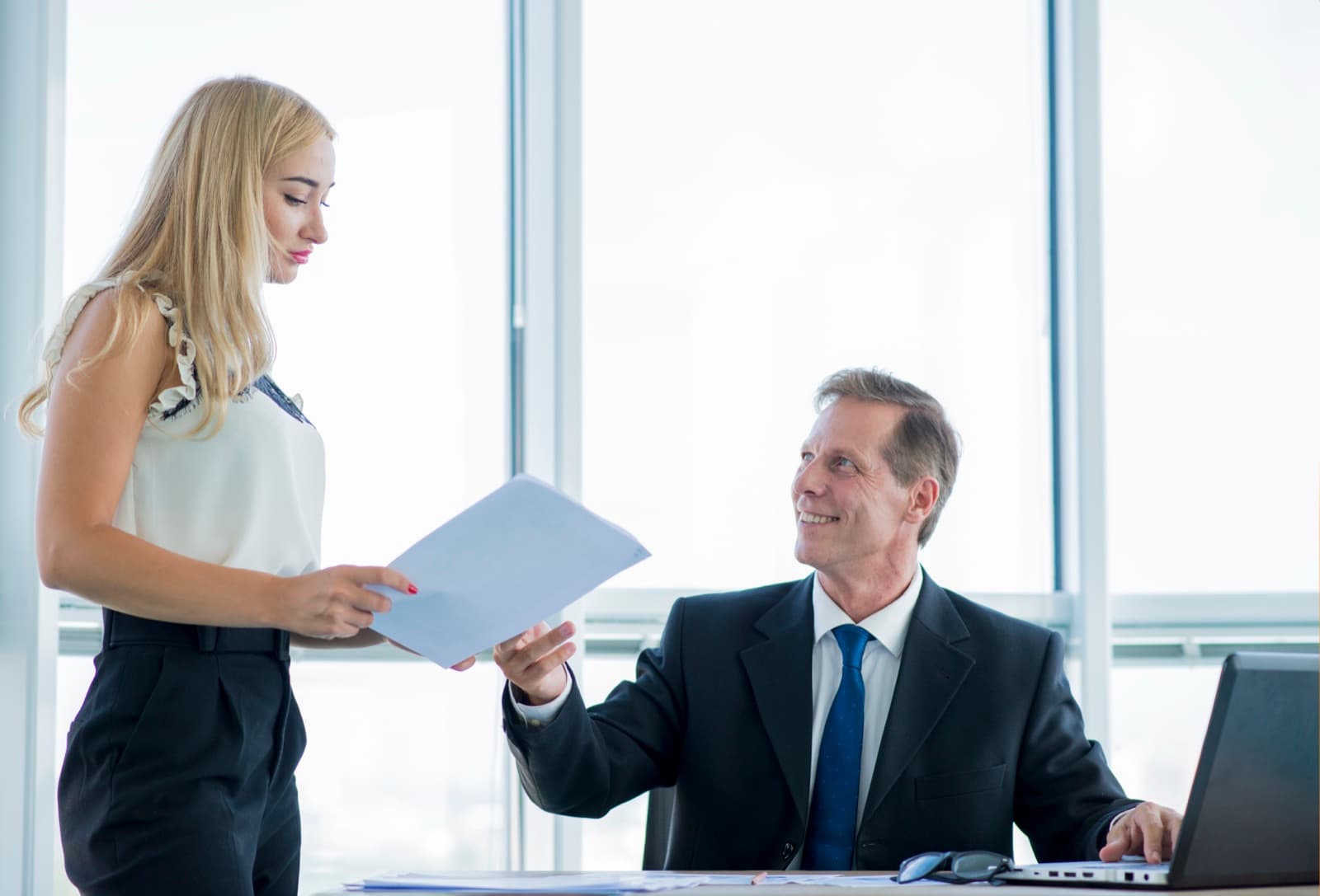 One person handing documents to another in an office