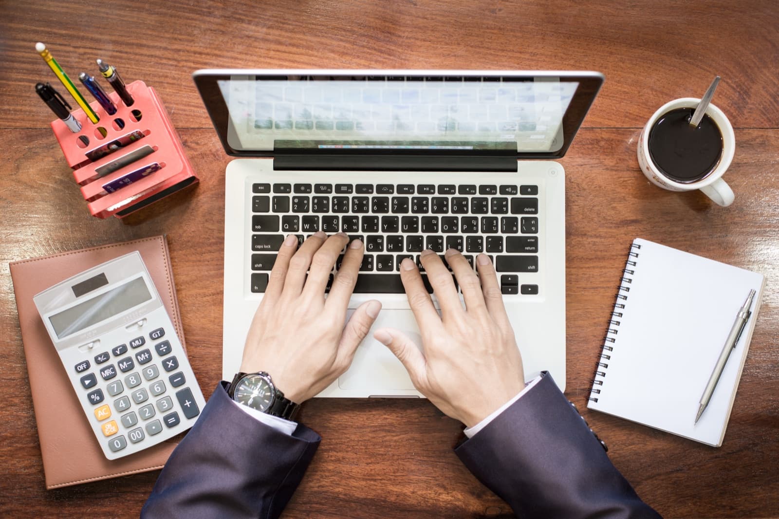 Hands working at a laptop with a calculator on a desk