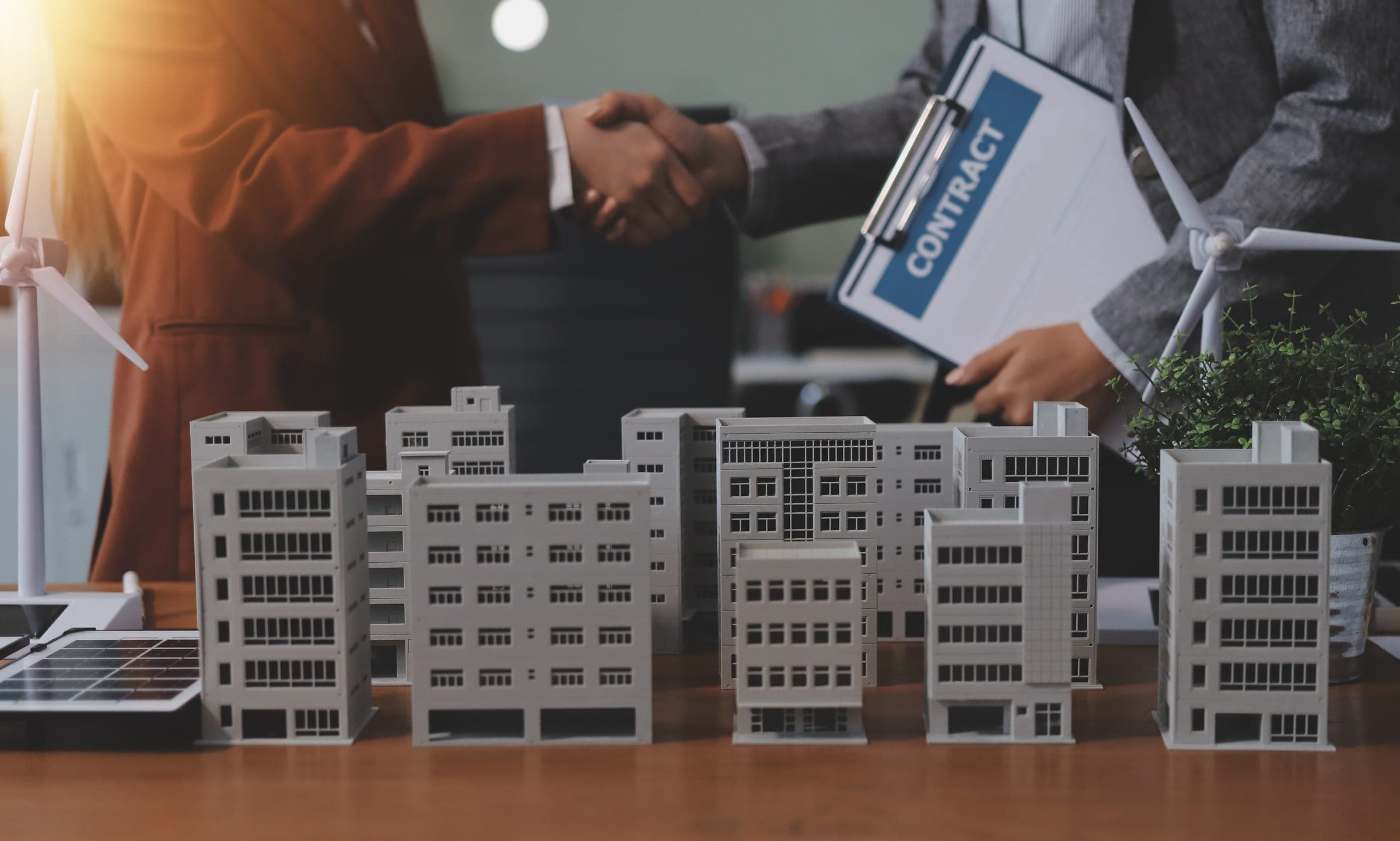 Business colleagues shaking hands over commercial property model.
