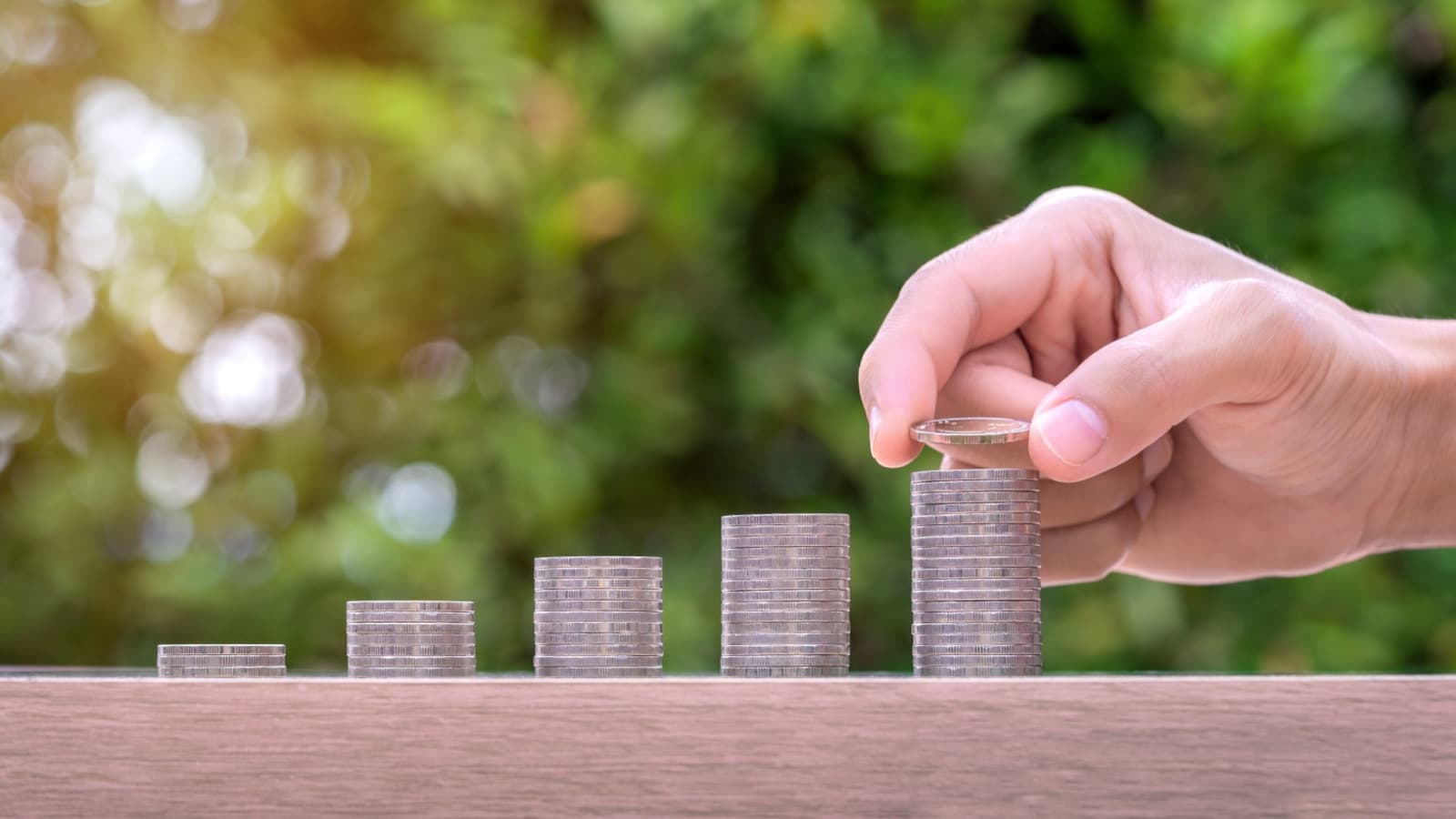 A hand adding a coin to growing stacks of coins