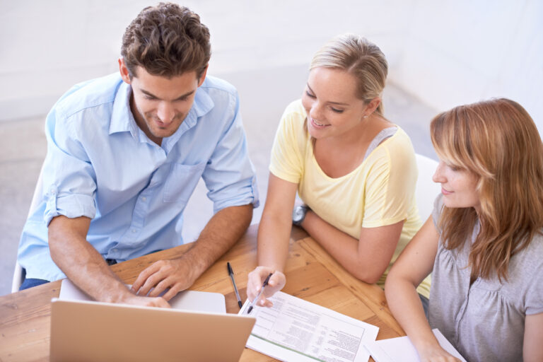 Three people discussing family trust distributions in Australia with a laptop and documents.